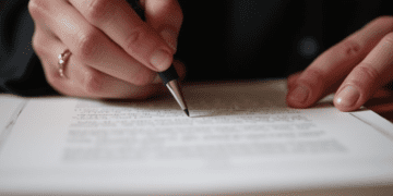 A close-up photograph of an author's hands signing a publishing contract