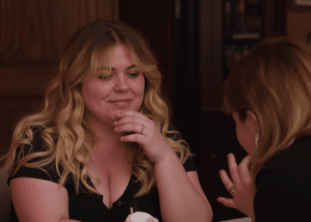 Author Colleen Hoover smiles while signing a book for a fan at an event.