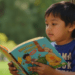 oung Filipino child reading a colorful storybook outdoors